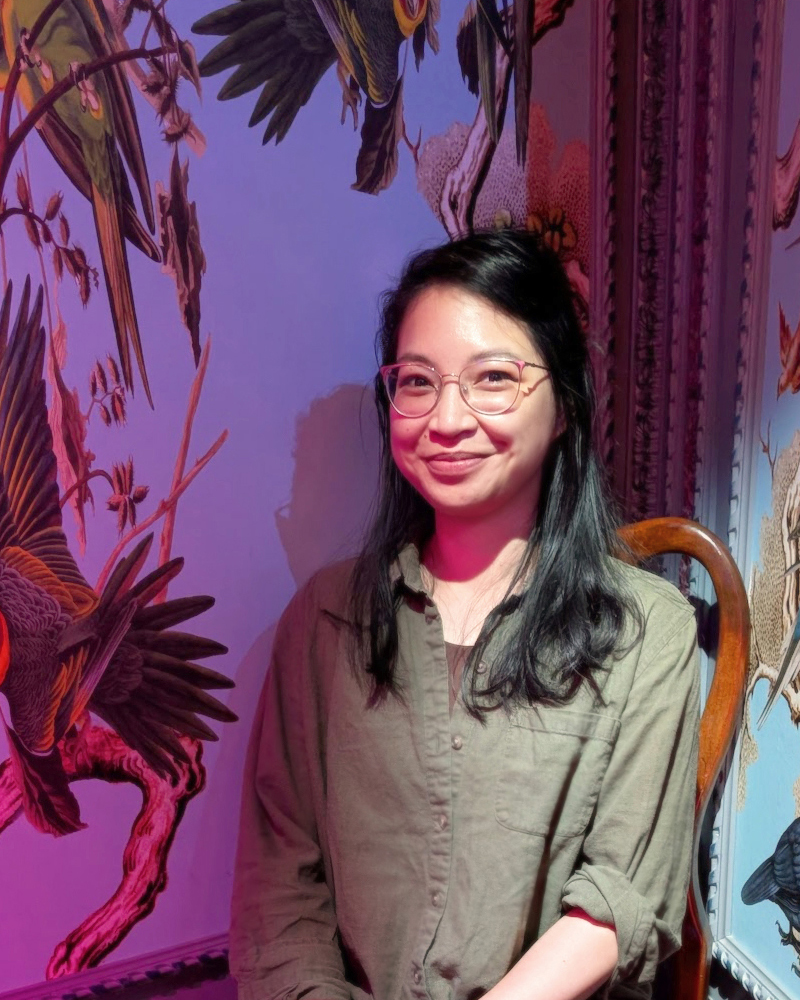 portrait of Denise Magdale smiling against a wallpapered background depicting birds and flowers